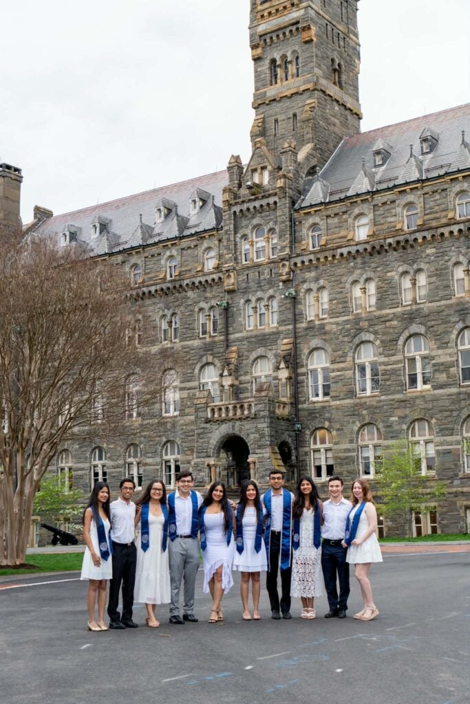 Priyasha stands with nine friends in graduation regalia in front of Georgetown's Healy Hall.