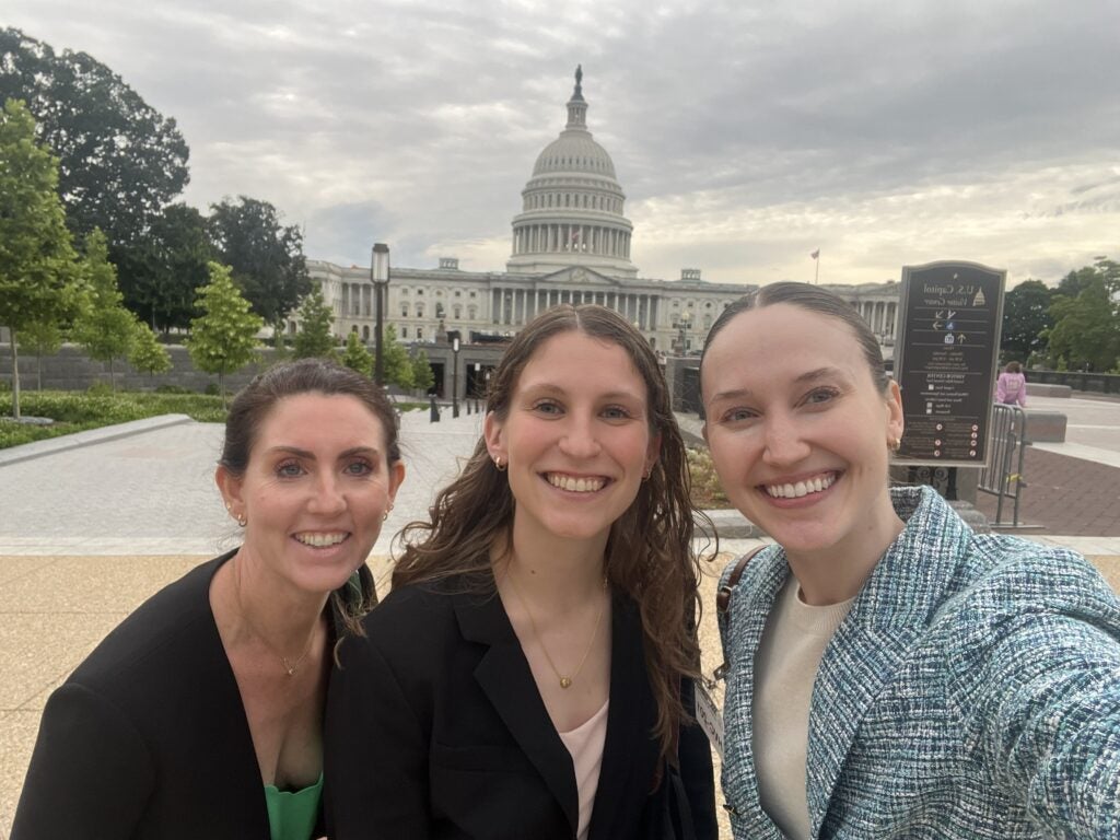 Three women appear in front of the U.S. Capitol in a selfie-style photo.