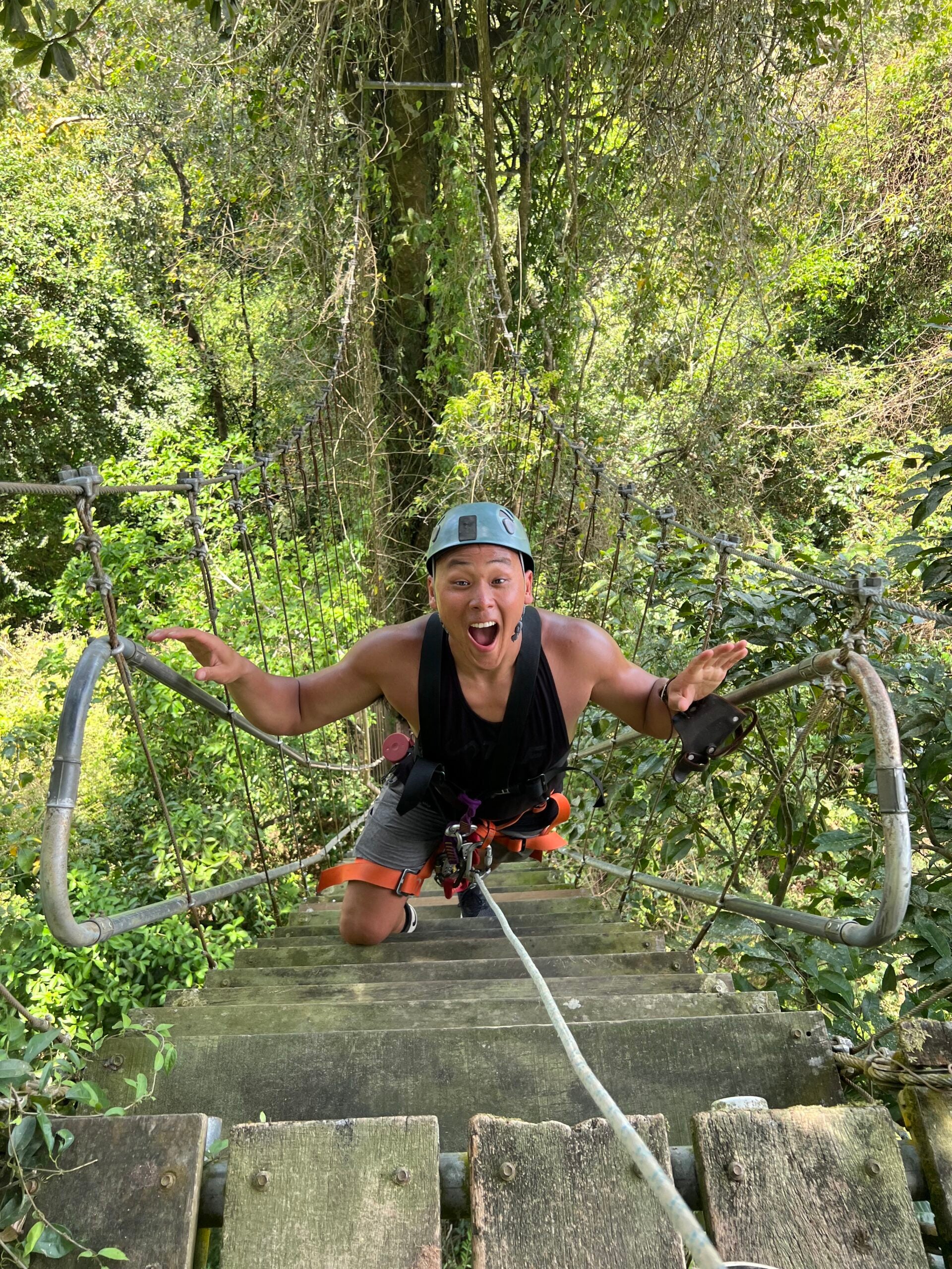 Anthony Choi wears ziplining gear while climbing stairs in the treetops of a forest.