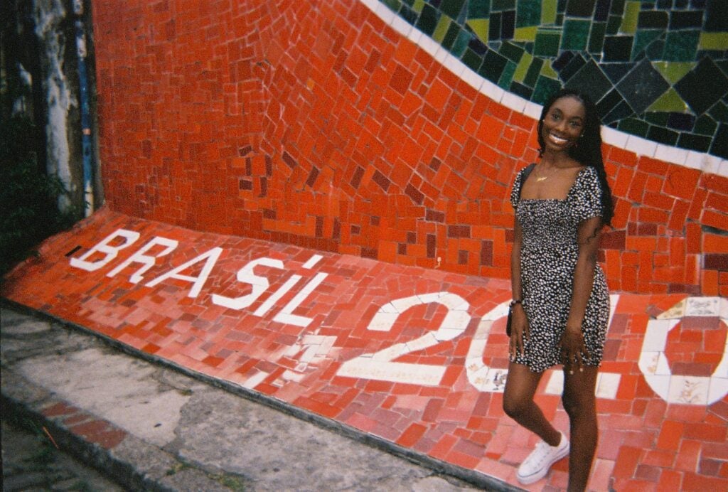 Jennifer Ayarkwa stands in front of a red- and white-tiled mosaic that spells out "Brasil 2010"