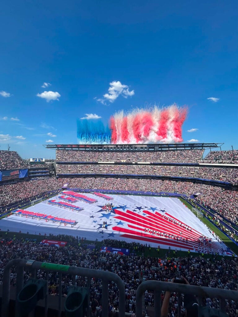 A photo of the Lincoln Financial Field during a Fourth of July performance during the FIFA World Cup. Red, white and blue decor is seen on the field, and colored smoke shoots from the stadium into the sky.