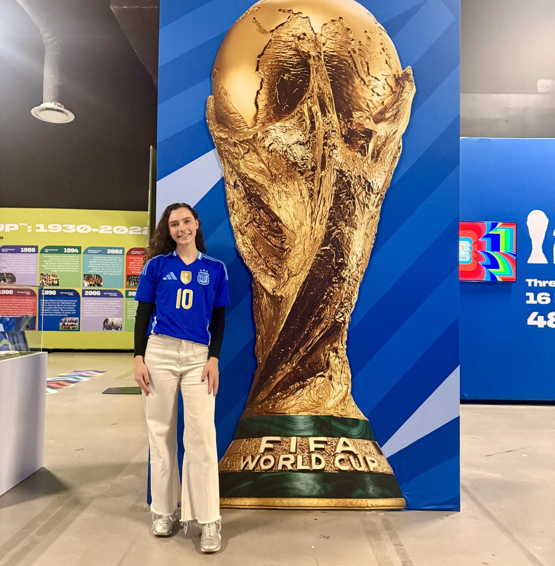 Georgetown Ph.D. student Rachel Beatty in front of a poster of a FIFA trophy.
